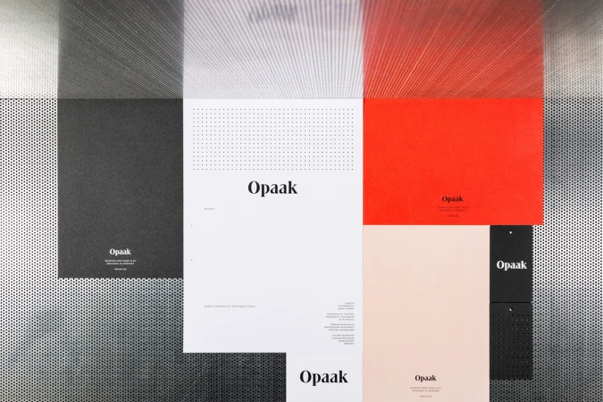 Flat lay of corporate stationery branding materials featuring the Opaak logo on white, black, red, and peach paper against a perforated metal texture