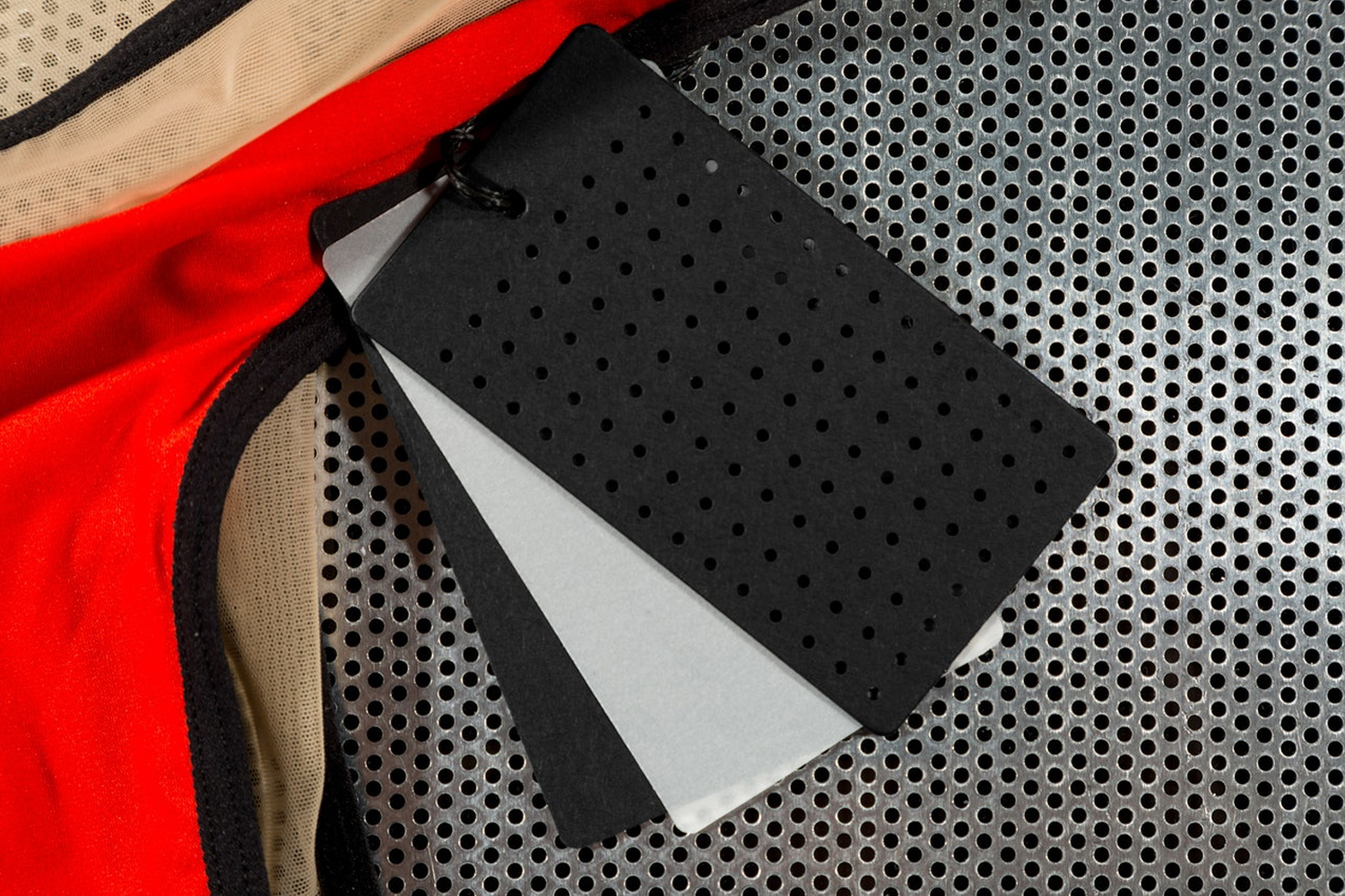 Close-up of perforated hang tags attached to a red and beige garment resting on a textured metal surface.