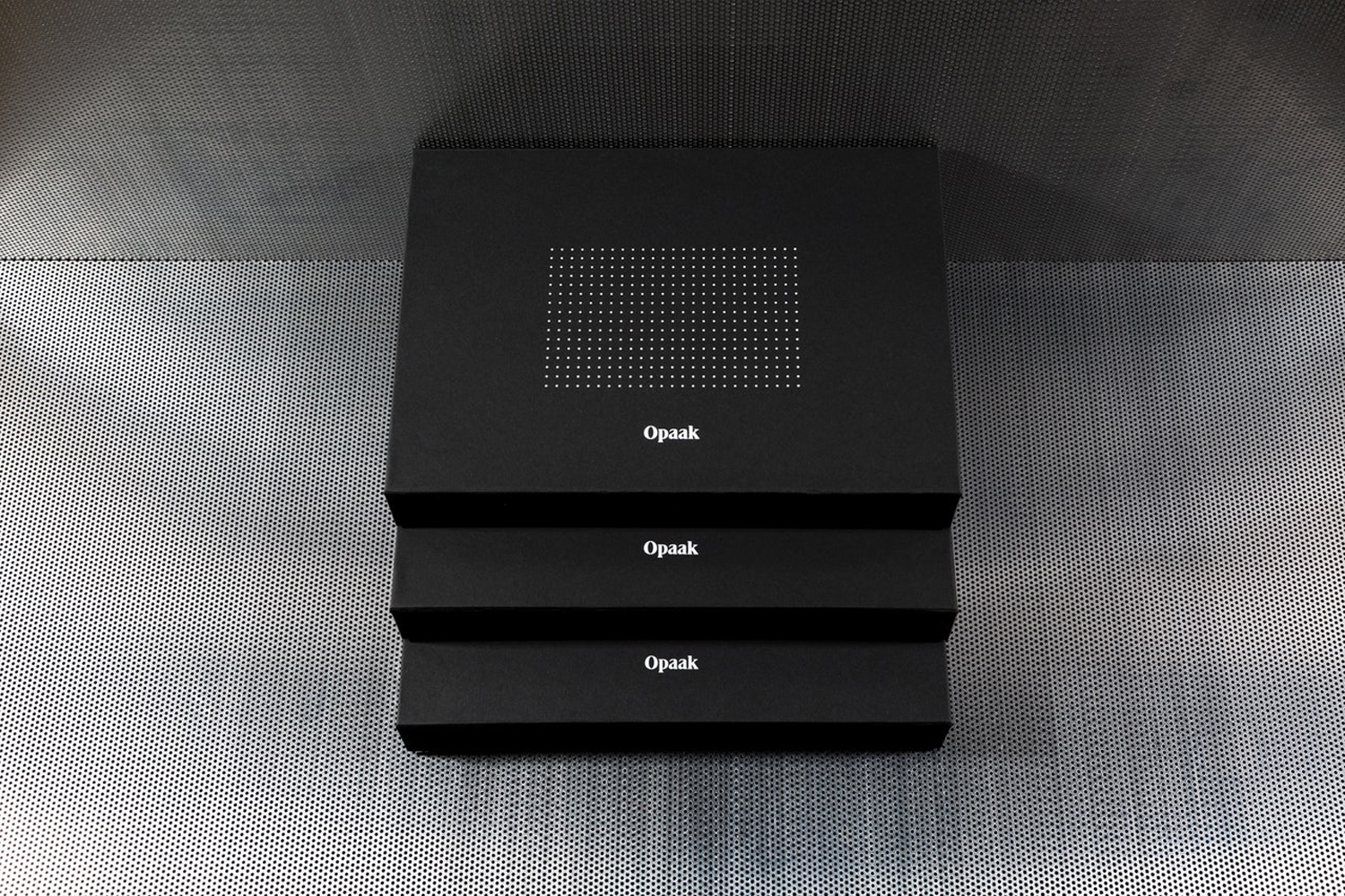 Three stacked matte black boxes featuring white typography and a dotted grid pattern against a textured metal background.