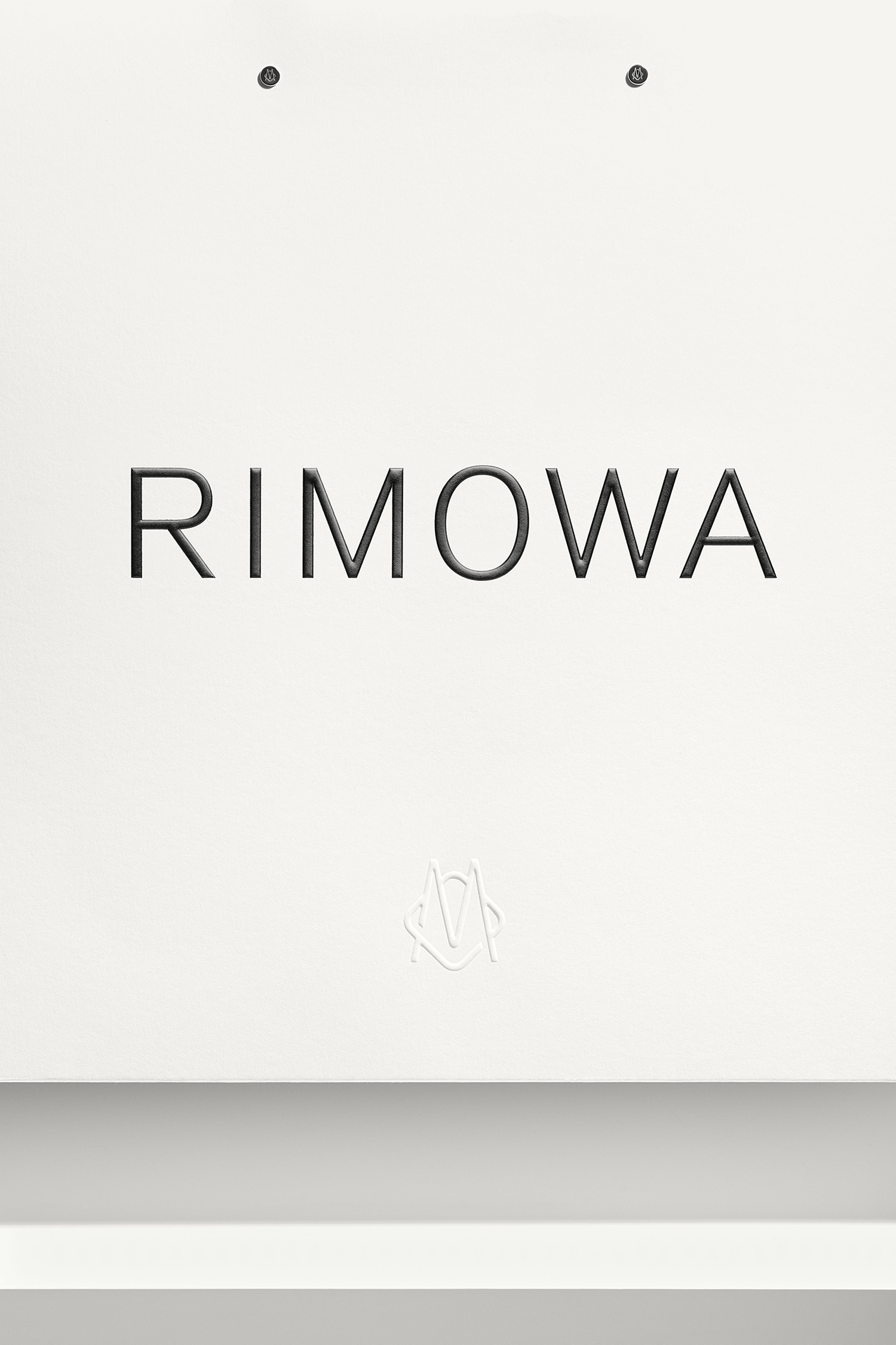 RIMOWA brand identity showcase featuring uppercase logotype centered on a clean white background with subtle grey surface below