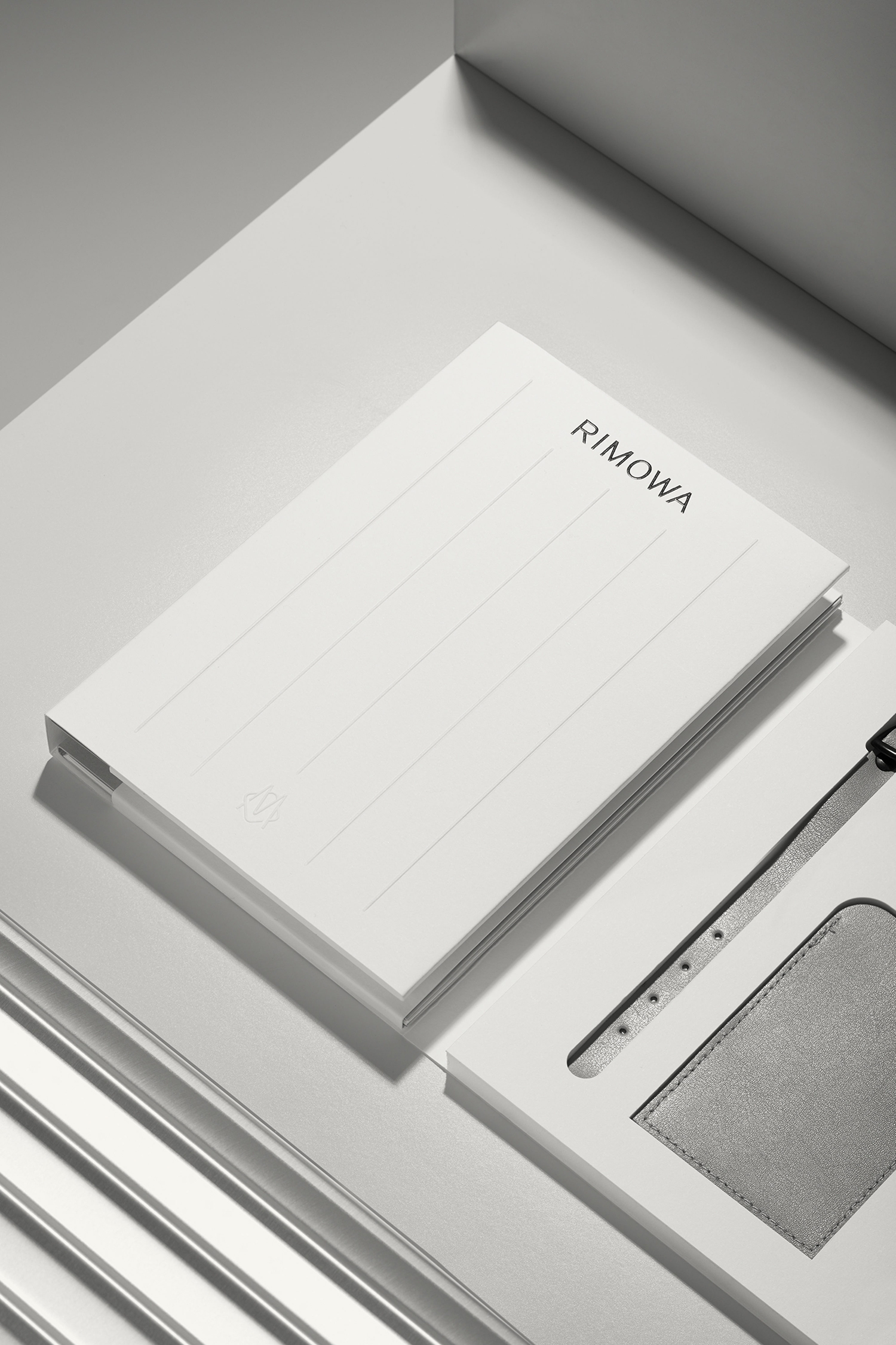 White RIMOWA branded notebook resting on a grey geometric surface with clean modern lines