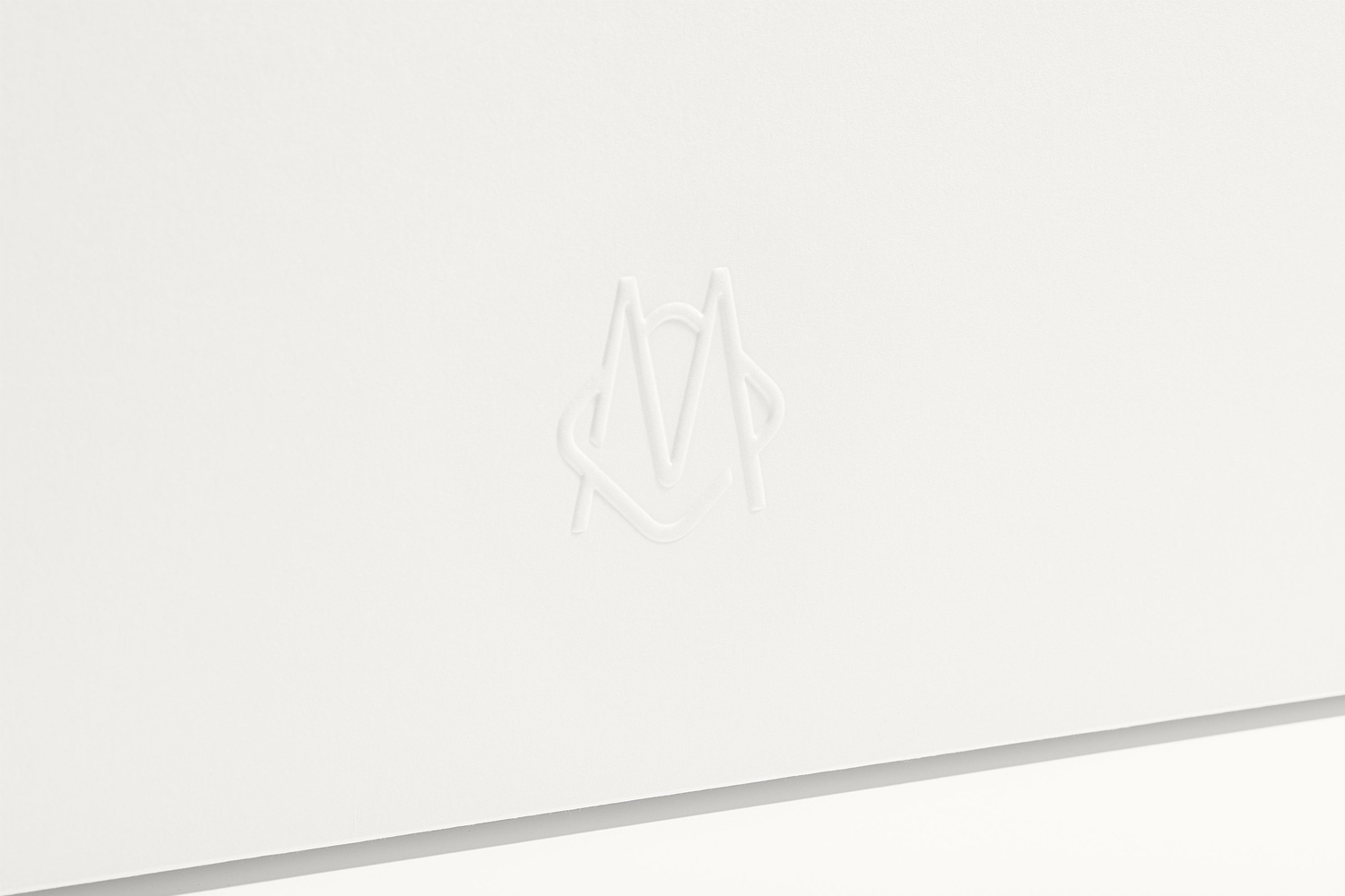 Close-up of a white embossed monogram logo on a clean white paper surface with soft lighting.