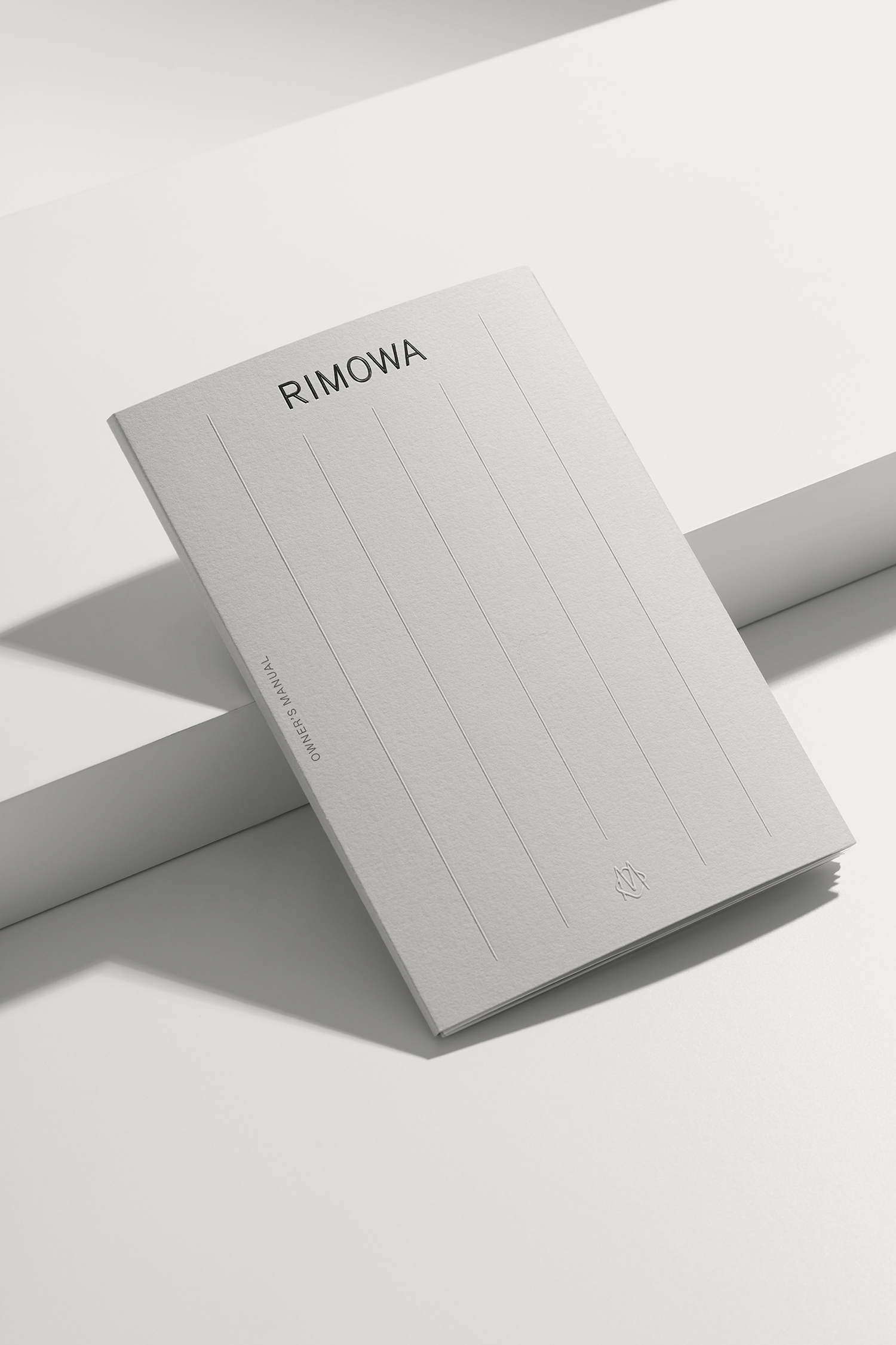 RIMOWA branded manual booklet resting on angled white stepped platform surfaces under soft studio lighting.