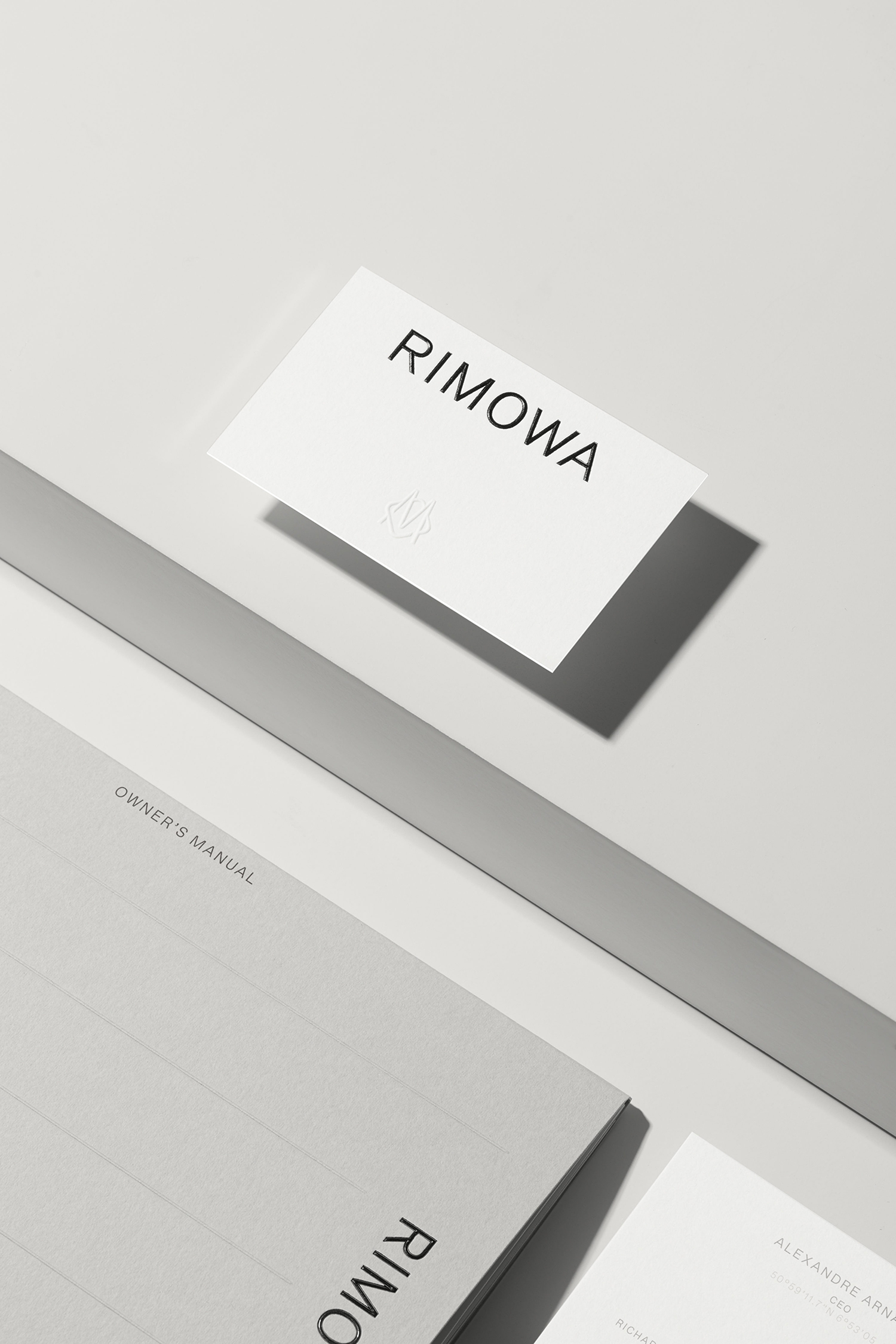 Minimalist graphic design identity for RIMOWA showing branded business cards and collateral on a neutral grey surface.