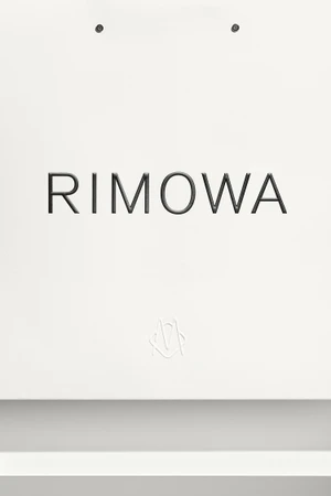 RIMOWA brand identity showcase featuring uppercase logotype centered on a clean white background with subtle grey surface below