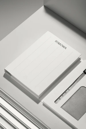 White RIMOWA branded notebook resting on a grey geometric surface with clean modern lines