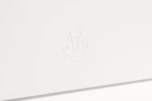 Close-up of a white embossed monogram logo on a clean white paper surface with soft lighting.