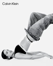 Rosalia lying on a white studio background wearing Calvin Klein black underwear and baggy denim jeans