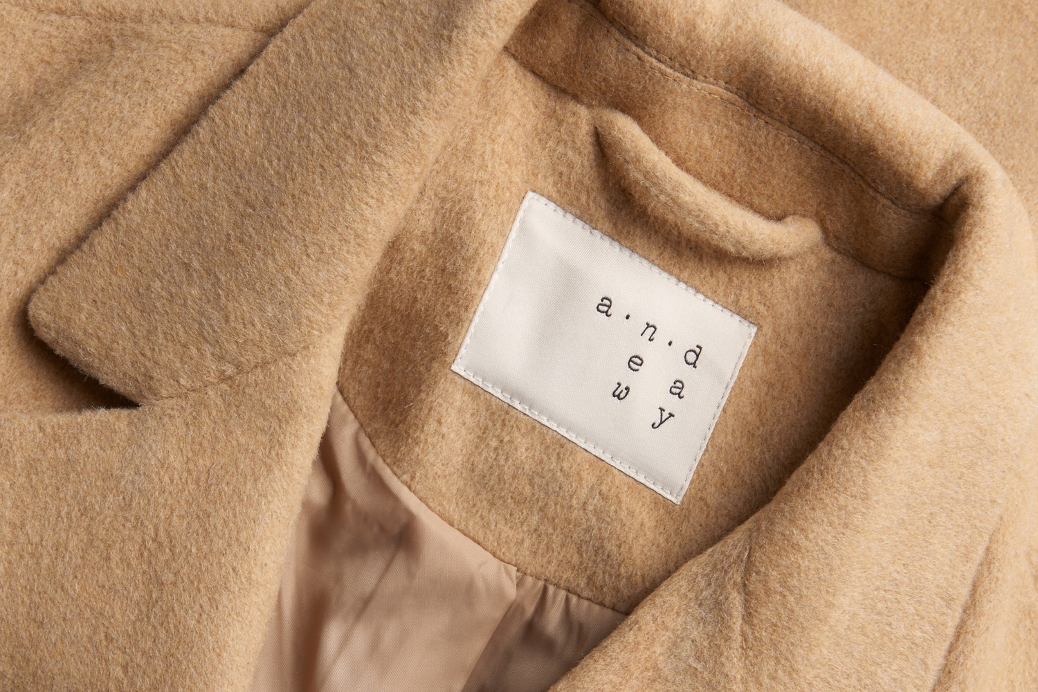 Close-up of a tan wool coat collar showing a white interior brand label reading a new day