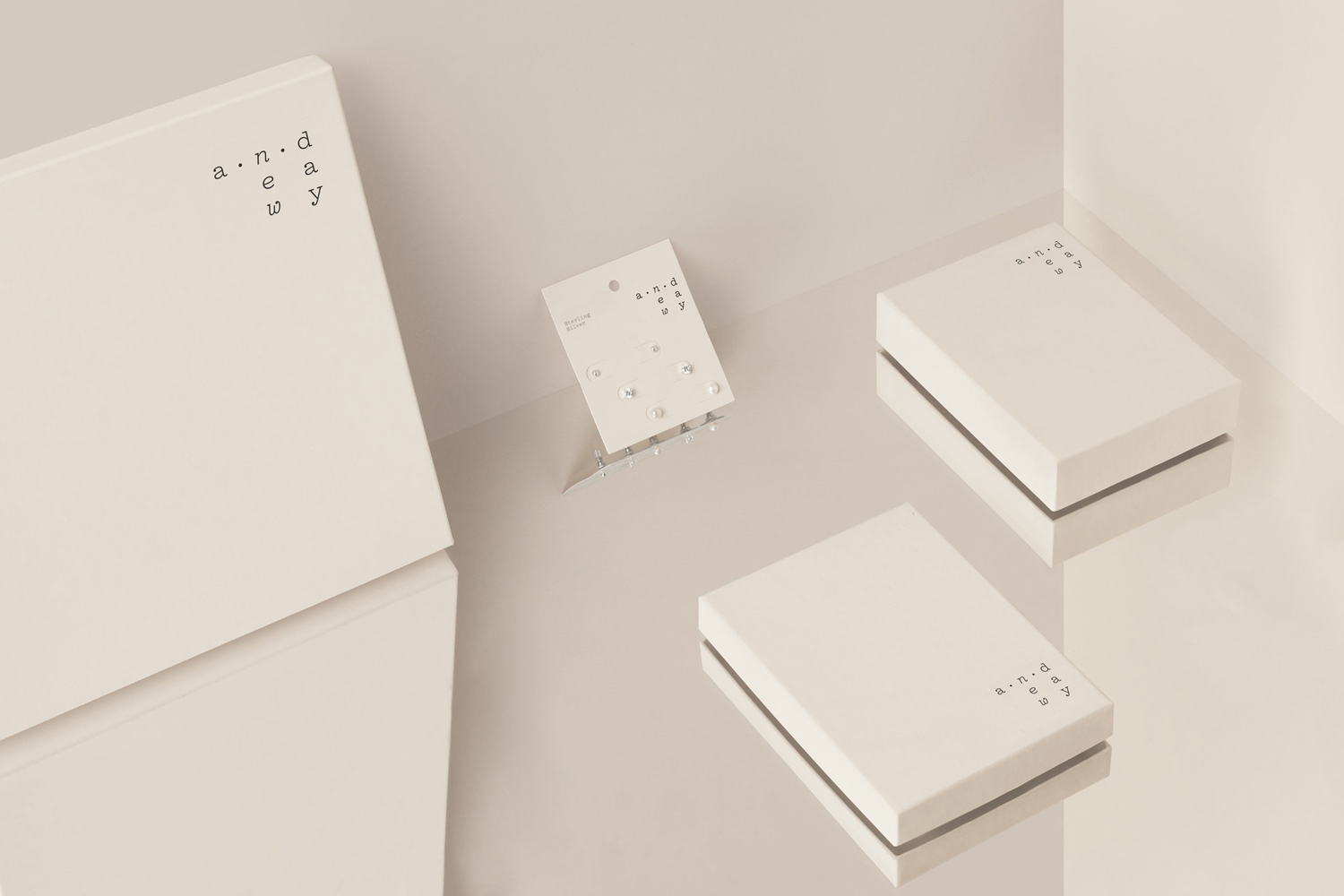 Minimalist product photography featuring white packaging boxes and an earring display card on a reflective surface.