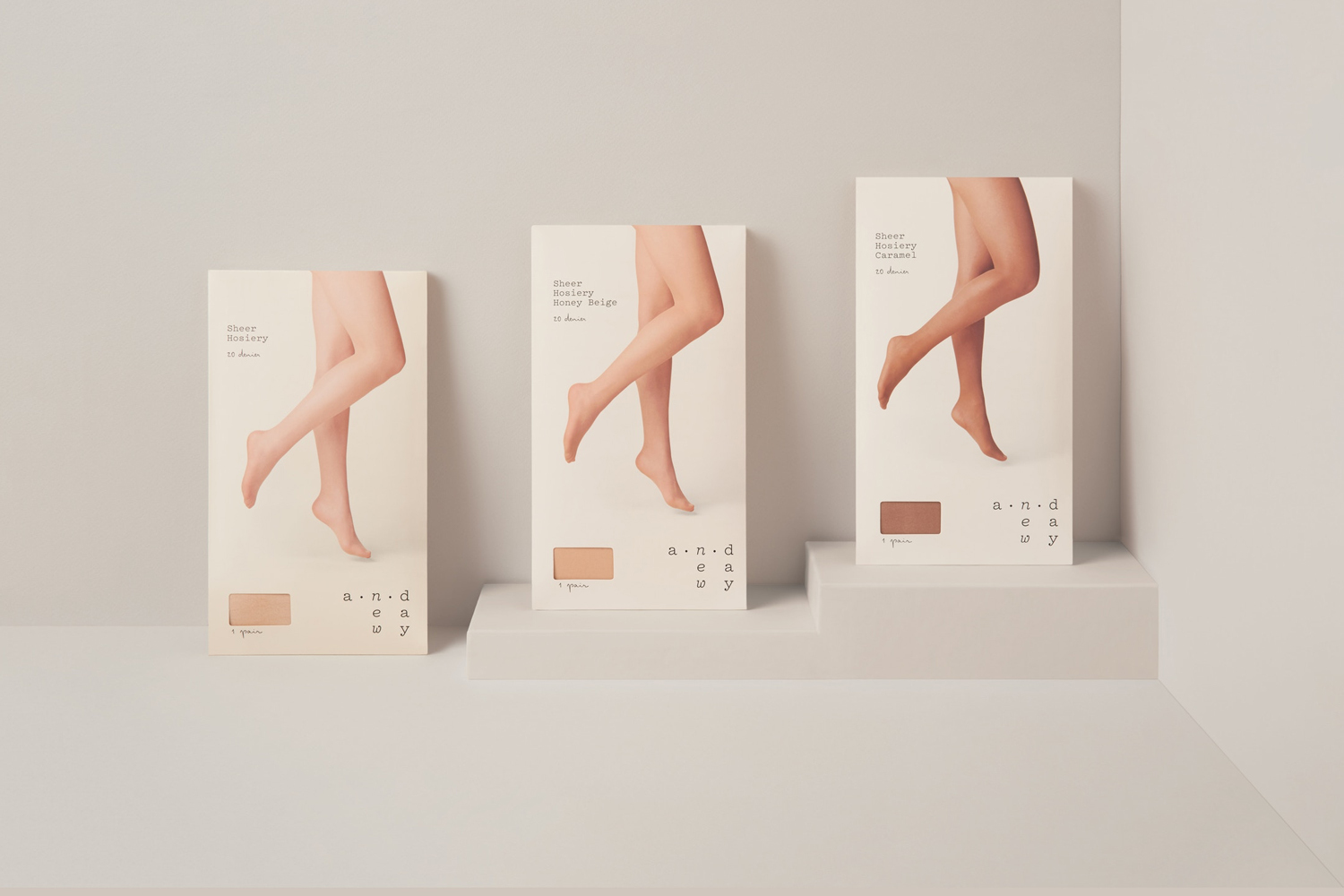 Three minimalist product packaging boxes for hosiery displayed on tiered light grey studio platforms