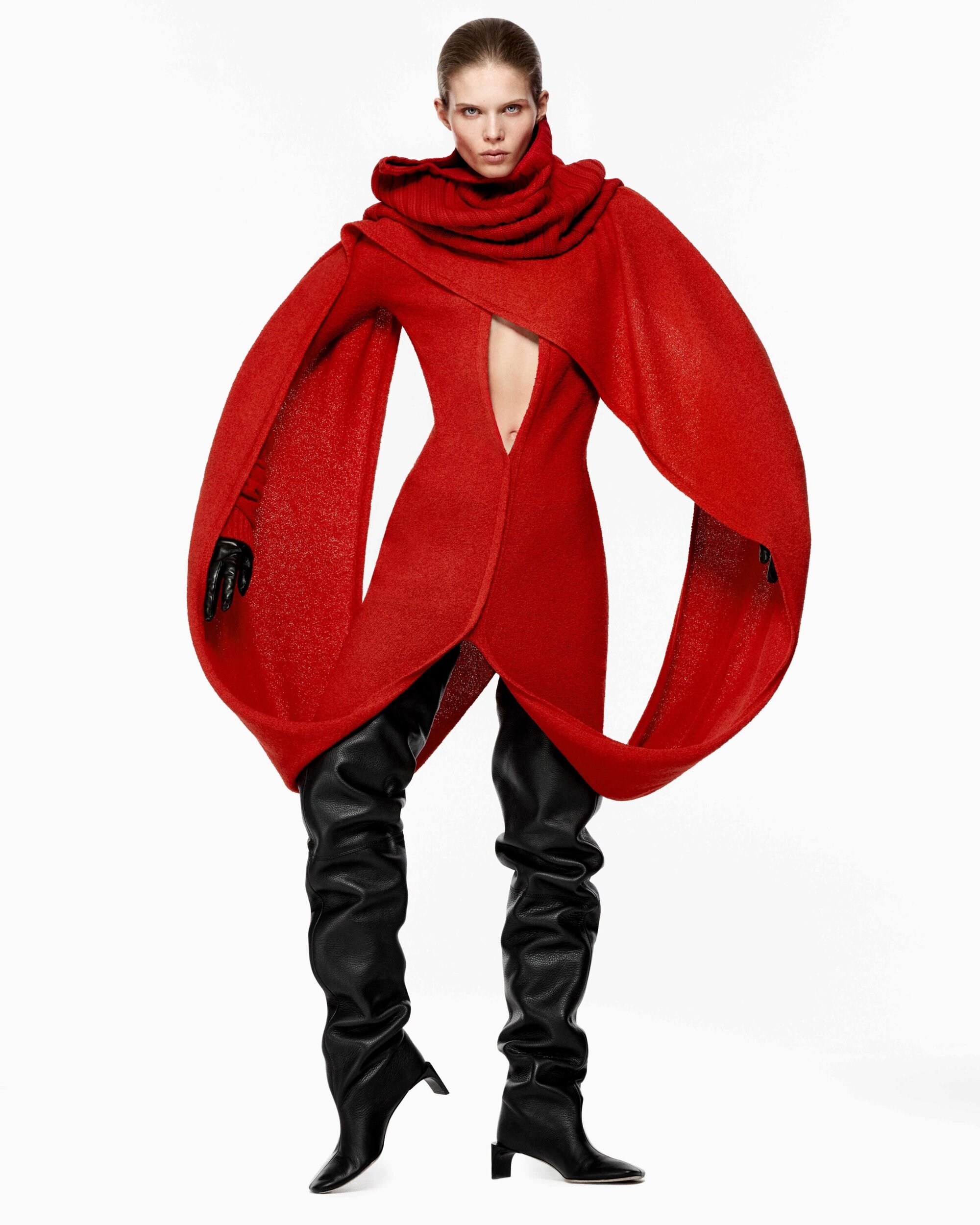 Model wearing a vibrant red structured wool dress with wide flared sleeves and black thigh-high boots against a plain white background