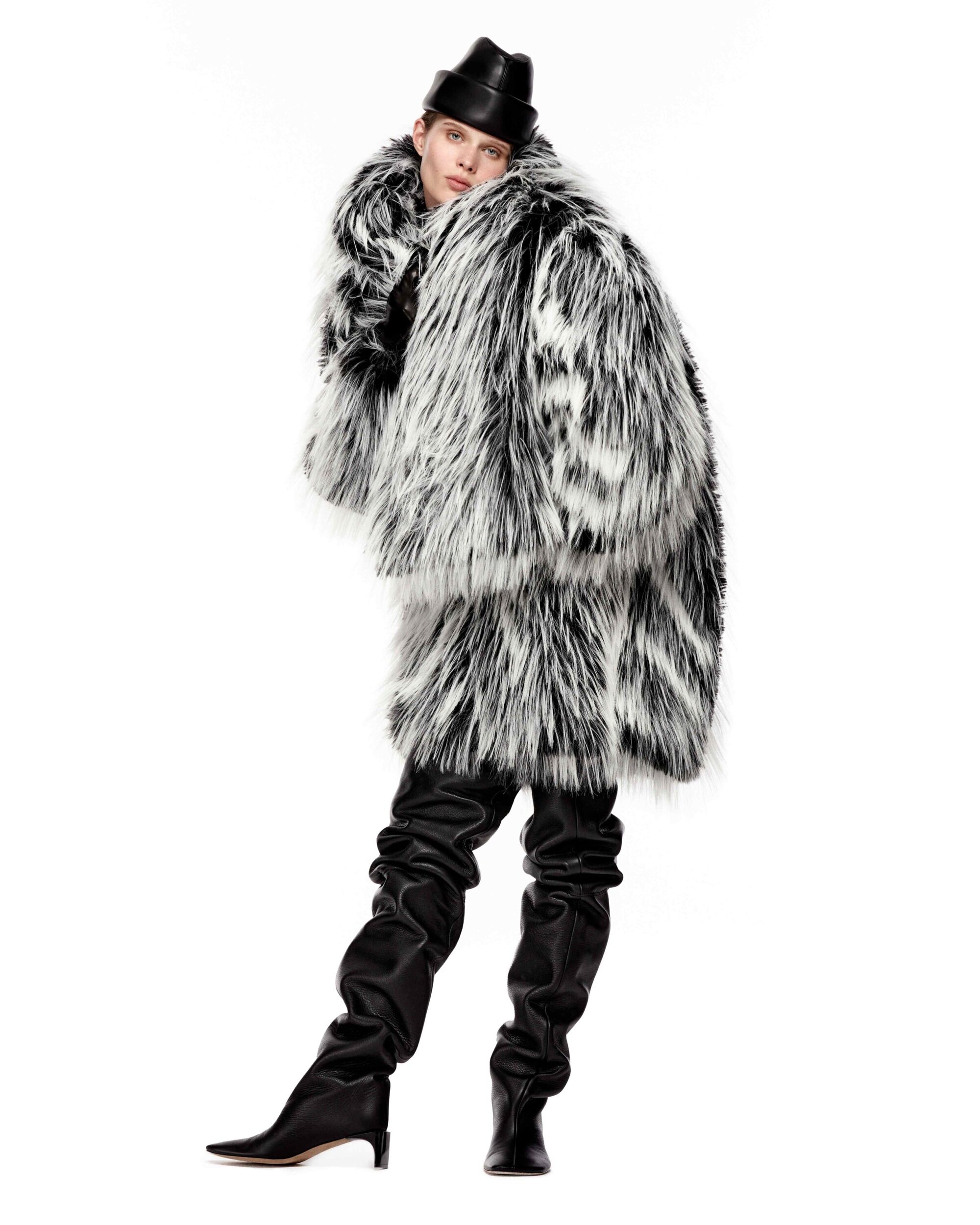 Model Ida Heiner wearing a voluminous black and white faux fur coat and thigh-high leather boots against a white backdrop.