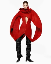 Model wearing a vibrant red structured wool dress with wide flared sleeves and black thigh-high boots against a plain white background