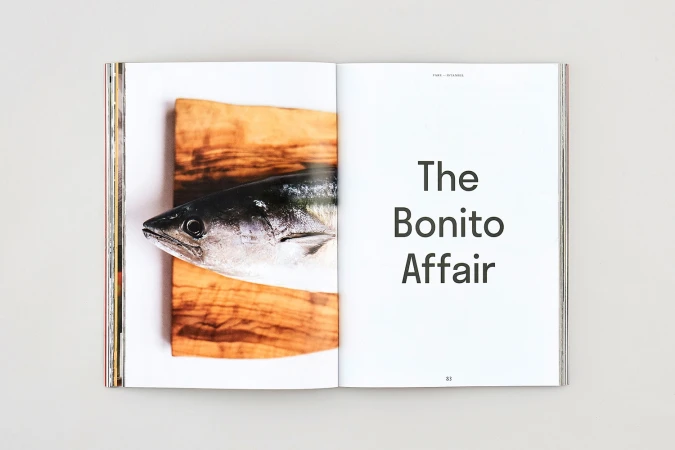 Open magazine spread showing a fresh fish on a wooden board on the left and typography reading The Bonito Affair on the right