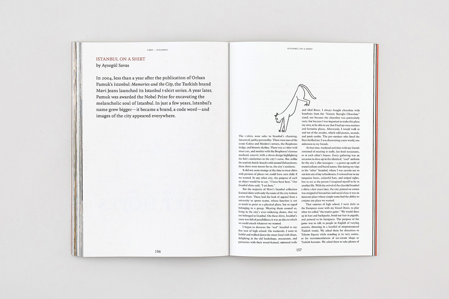Open magazine spread on a neutral surface featuring typographic layout, printed text columns, and a line drawing of a cat.