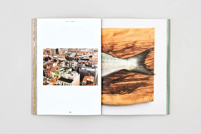 An open magazine showing a cityscape photograph on the left and a fish tail on a wooden board on the right.