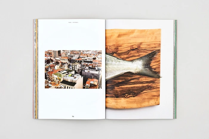 An open magazine showing a cityscape photograph on the left and a fish tail on a wooden board on the right.
