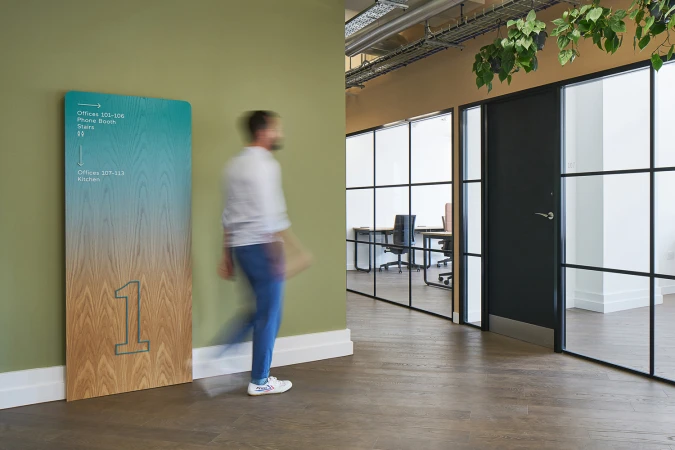 Motion blurred man walking past an olive green wall and wooden signage panel in an office interior