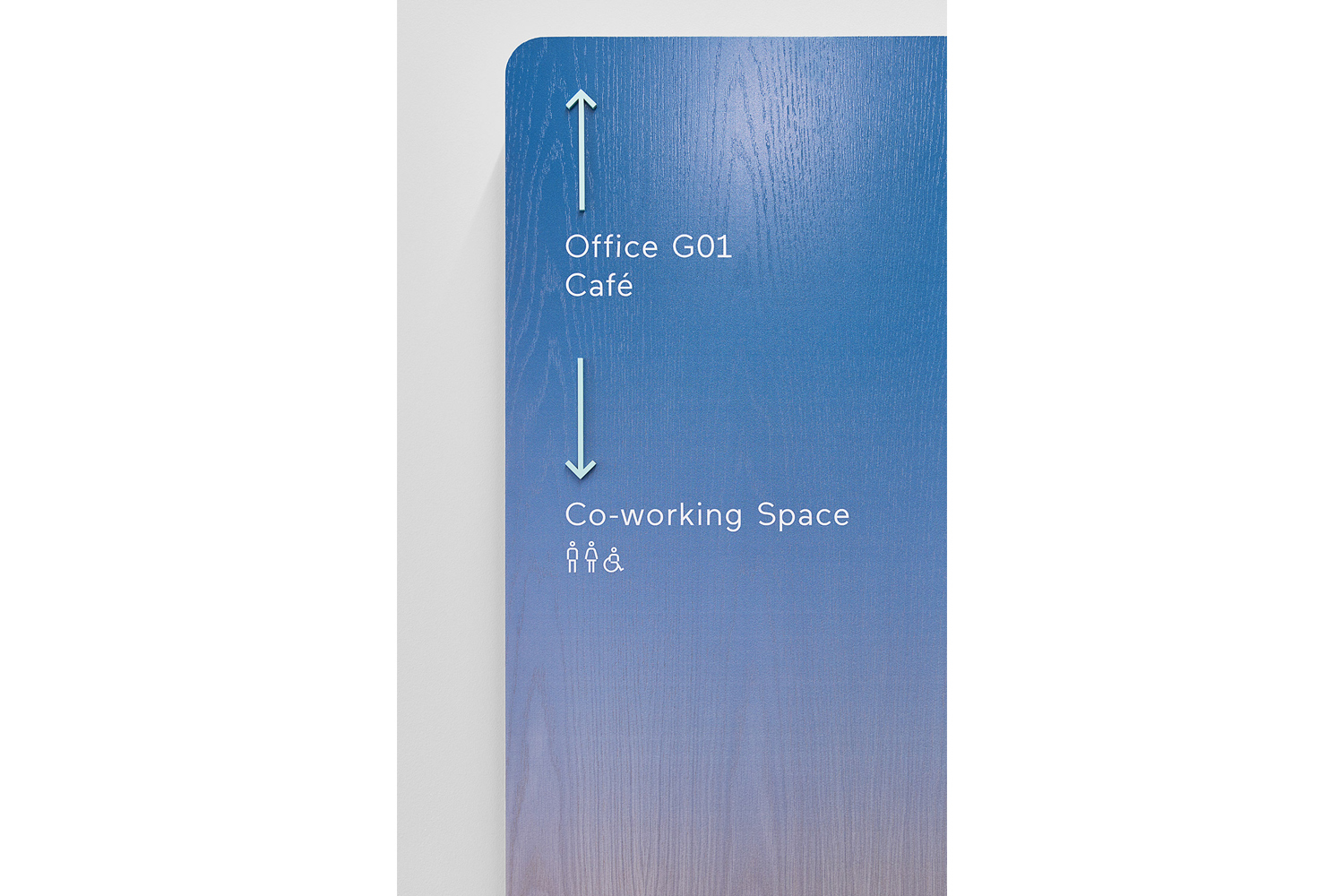 Blue gradient wooden directional signage panel with white text mounted on a plain white wall