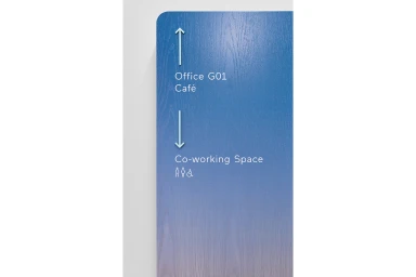 Blue gradient wooden directional signage panel with white text mounted on a plain white wall