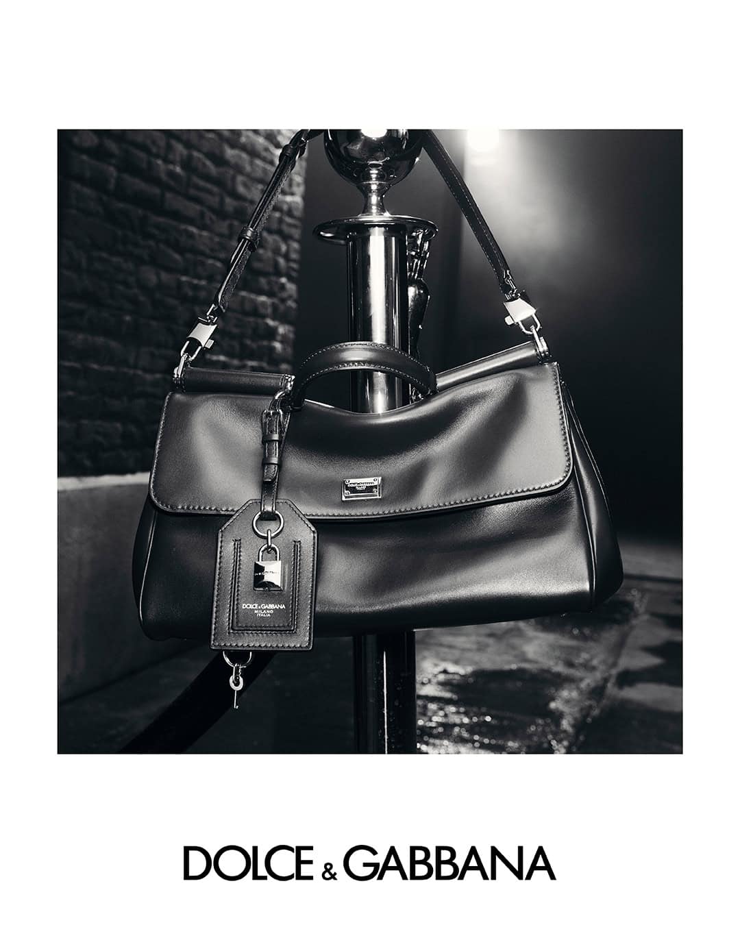 Monochrome product shot of a black leather handbag hanging from a chrome stanchion pole.
