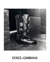 Black embellished leather boots with crystal details on a wet concrete surface for Dolce & Gabbana Fall 2025 campaign.