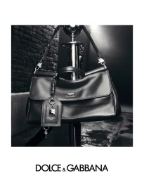 Monochrome product shot of a black leather handbag hanging from a chrome stanchion pole.