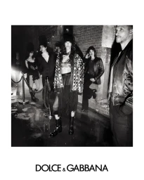 Black and white fashion campaign image featuring models in dark attire standing on a wet surface against a brick wall