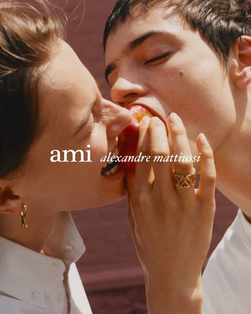 Close-up portrait of a woman and man biting into a red apple together for the Ami Fall 2025 ad campaign.