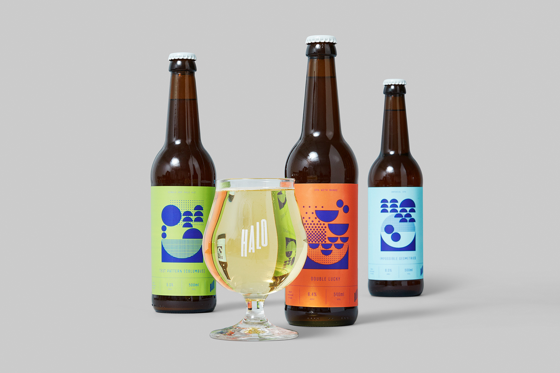 Three amber glass beer bottles with colourful geometric labels and a branded glass filled with golden beer against a plain light grey background.