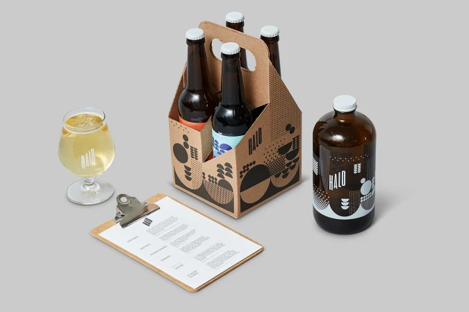Halo Brewery packaging identity featuring a 6-pack carrier, amber glass bottles, glass of beer, and a clipboard on grey seamless