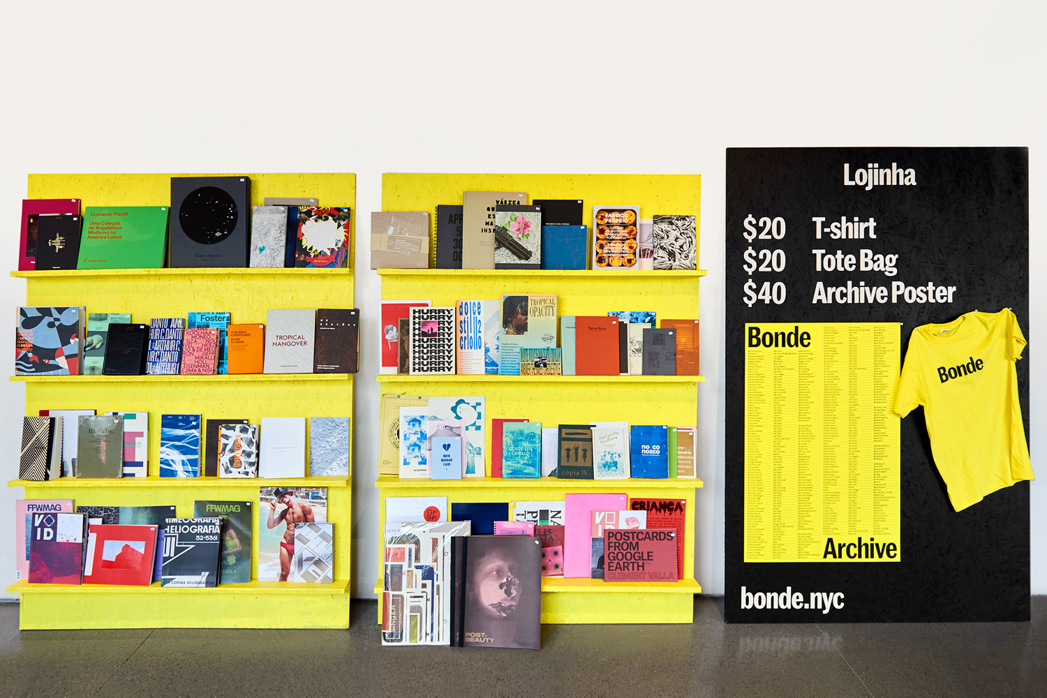 Yellow bookshelves displaying various art books next to a black sign with pricing for merchandise and archive posters.