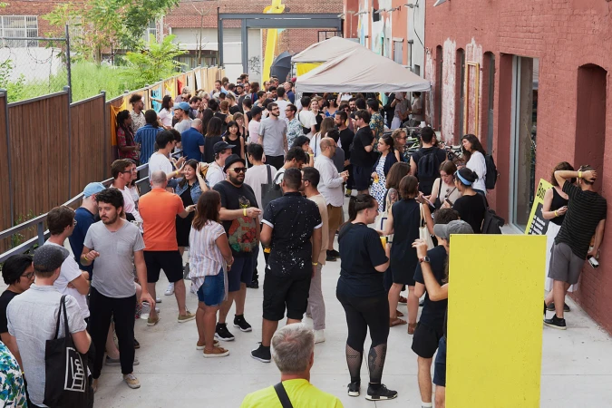 Large crowd of diverse people gathering outdoors in a narrow alleyway between red brick buildings during a daytime event by PORTO ROCHA.