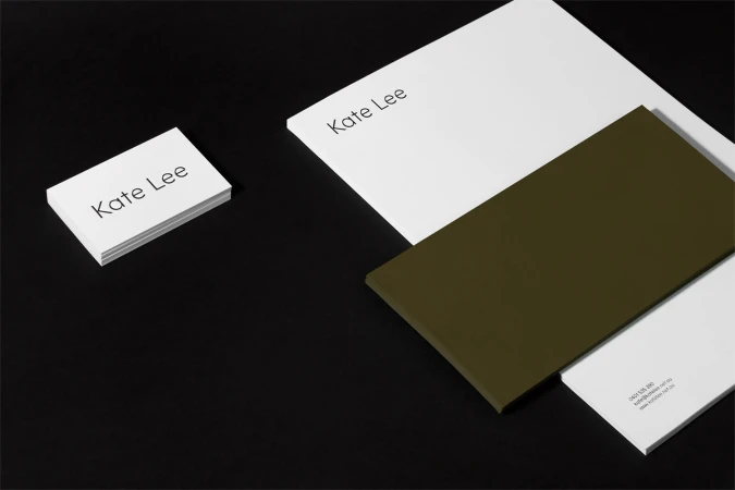 Minimalist brand identity stationery featuring stacked white business cards and letterhead with dark olive green elements on black