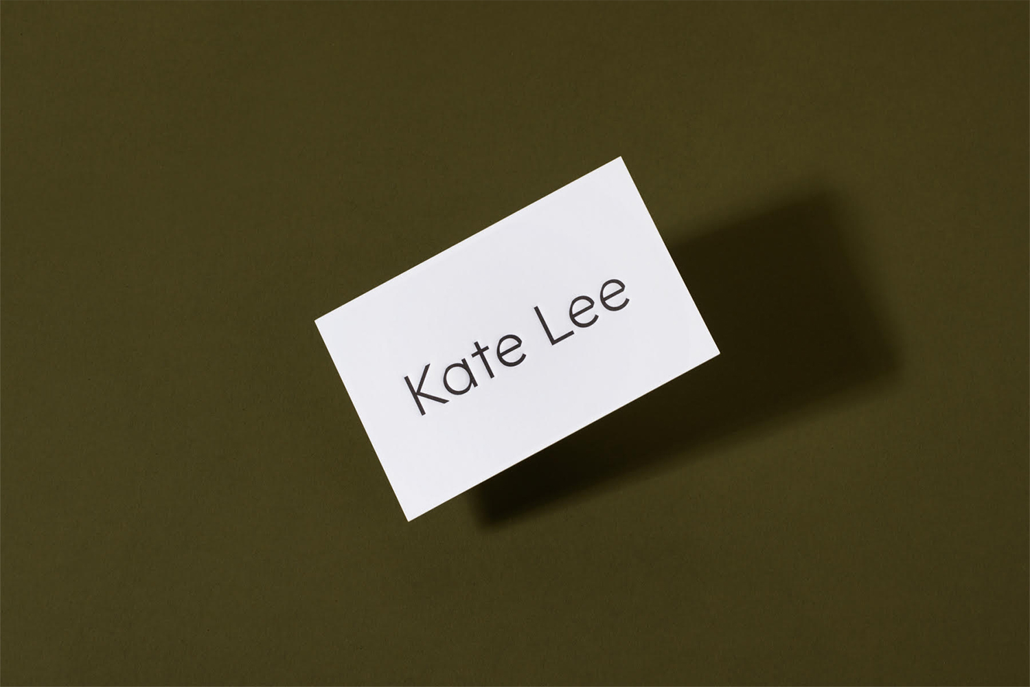 White business card with Kate Lee text casting a shadow on dark olive green background