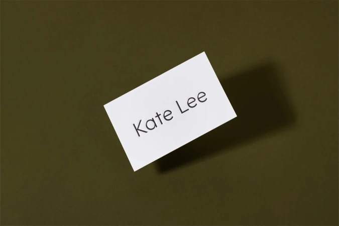 White business card with Kate Lee text casting a shadow on dark olive green background
