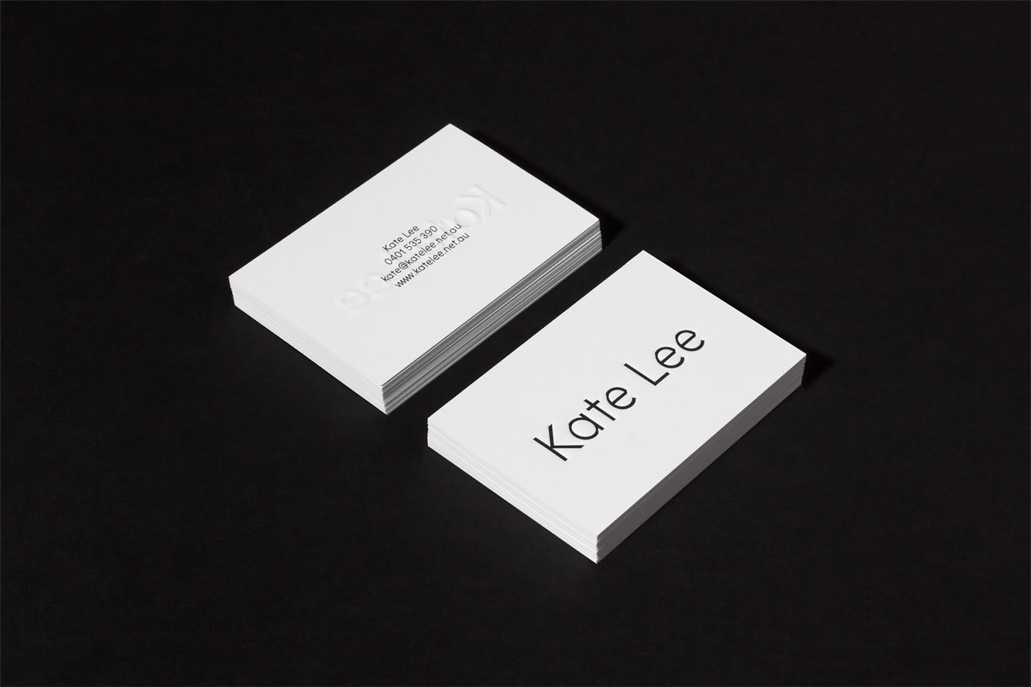 Two stacks of white business cards featuring minimalist typography on a dark surface.