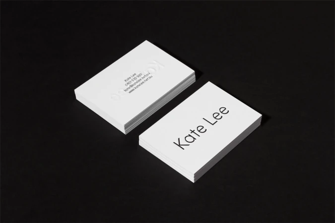 Two stacks of white business cards featuring minimalist typography on a dark surface.