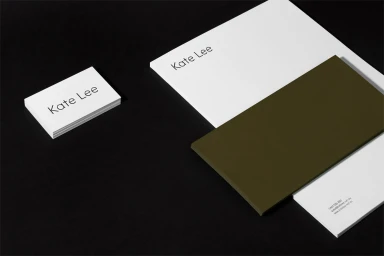 Minimalist brand identity stationery featuring stacked white business cards and letterhead with dark olive green elements on black