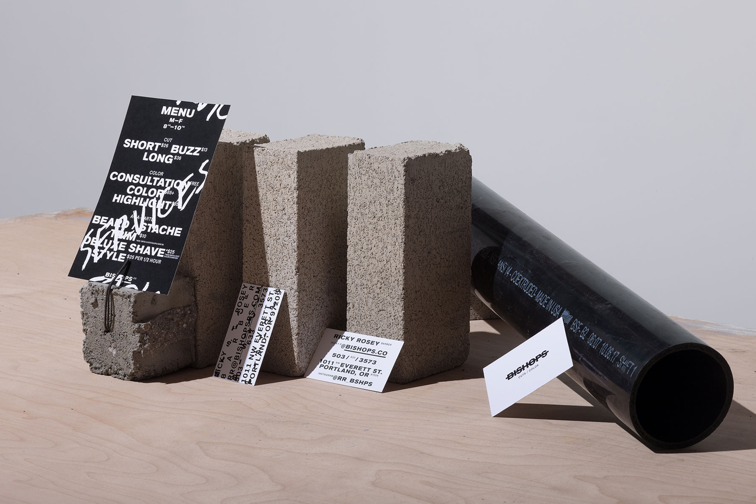 Bishops brand identity design featuring concrete blocks, business cards, a price menu, and a black pipe on wood.