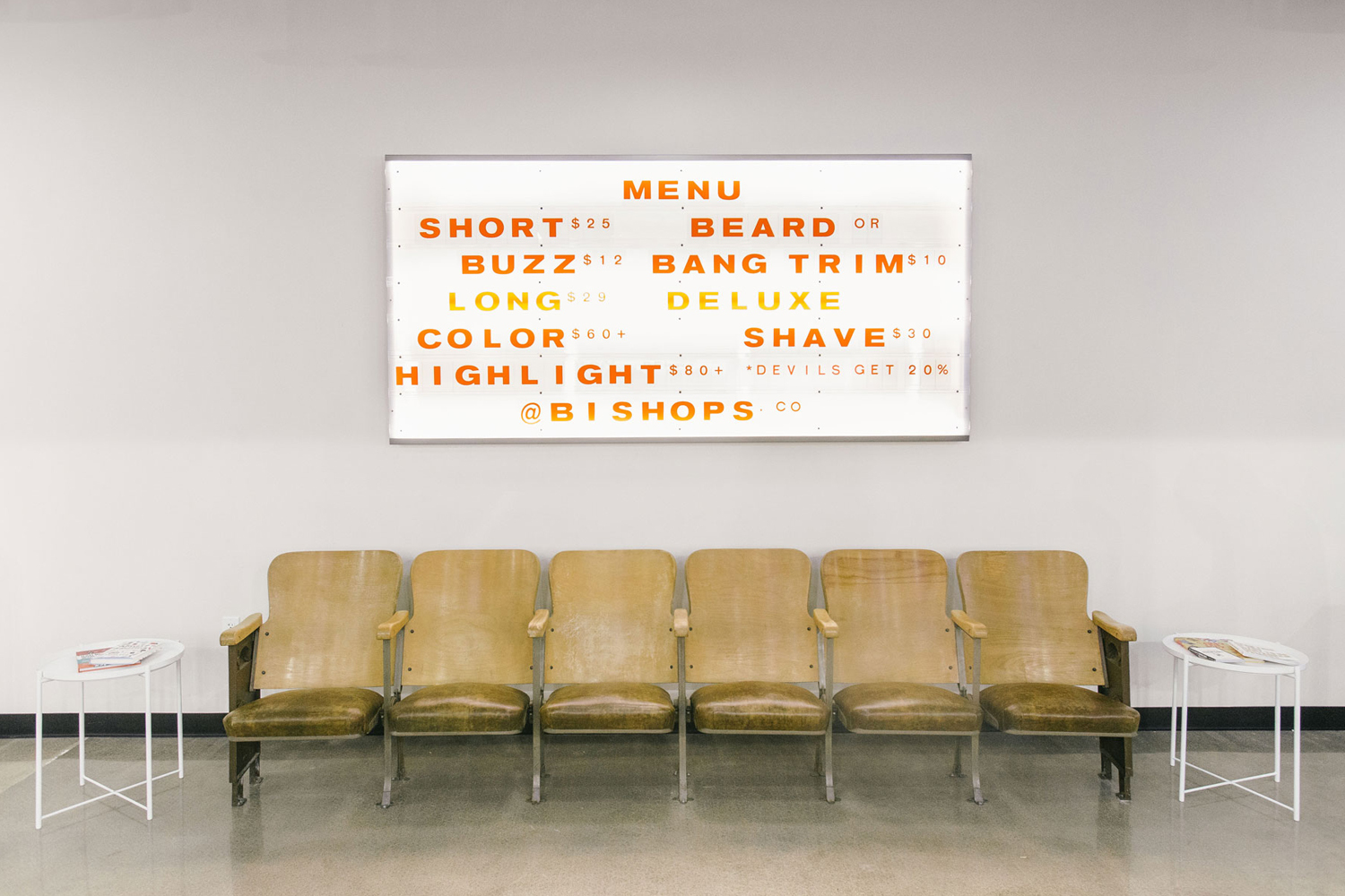 A row of wooden chairs beneath a lighted menu board displaying pricing and services for Bishops brand identity design