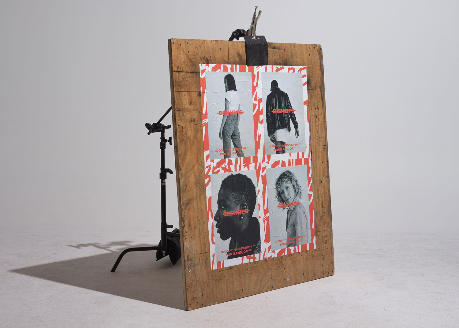 A large wooden board displaying a four-panel poster with red typographic branding is propped up in a bright studio space.
