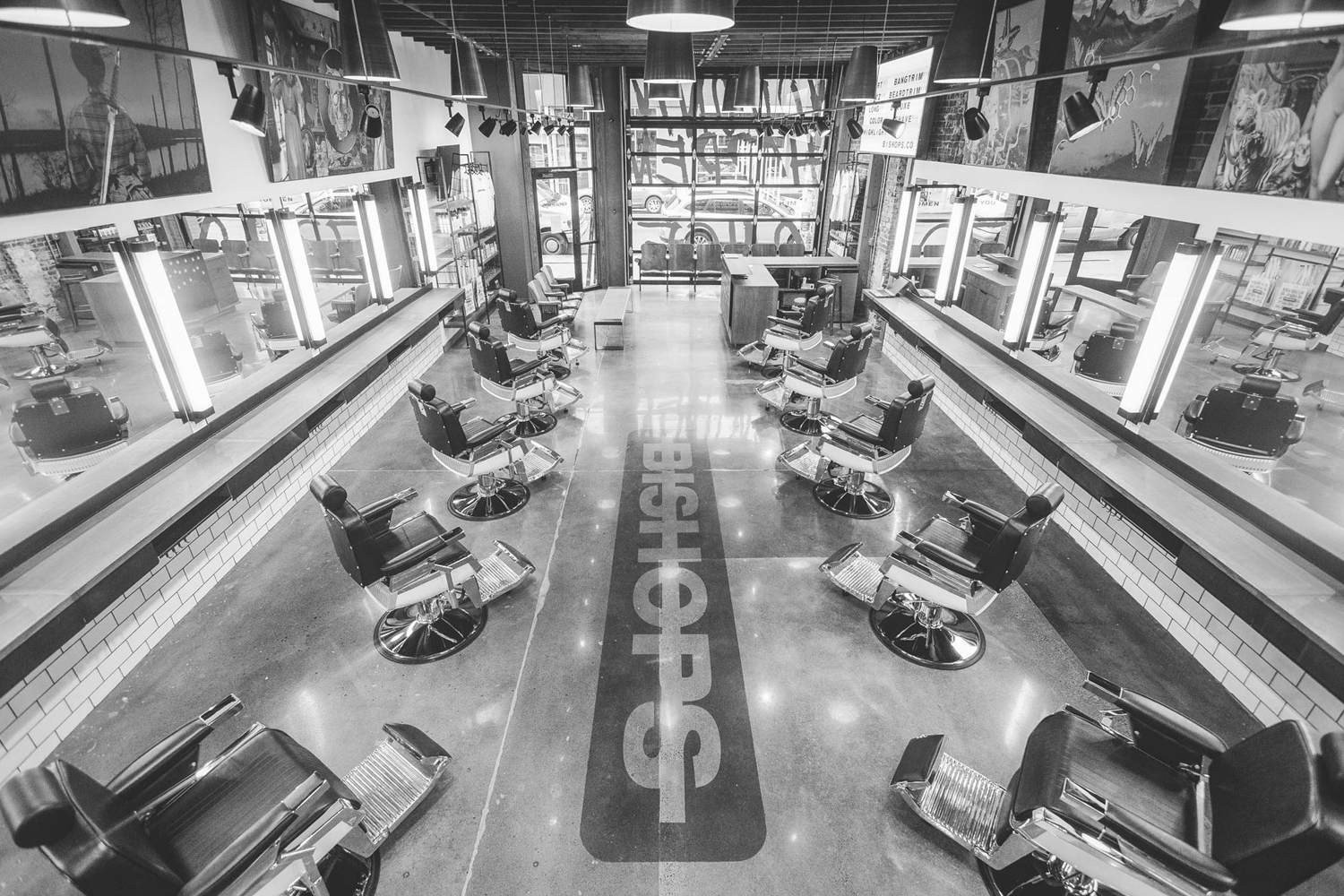 High-angle monochrome interior view of Bishops barbershop featuring rows of vintage barber chairs and glowing strip lights
