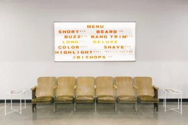 A row of wooden chairs beneath a lighted menu board displaying pricing and services for Bishops brand identity design
