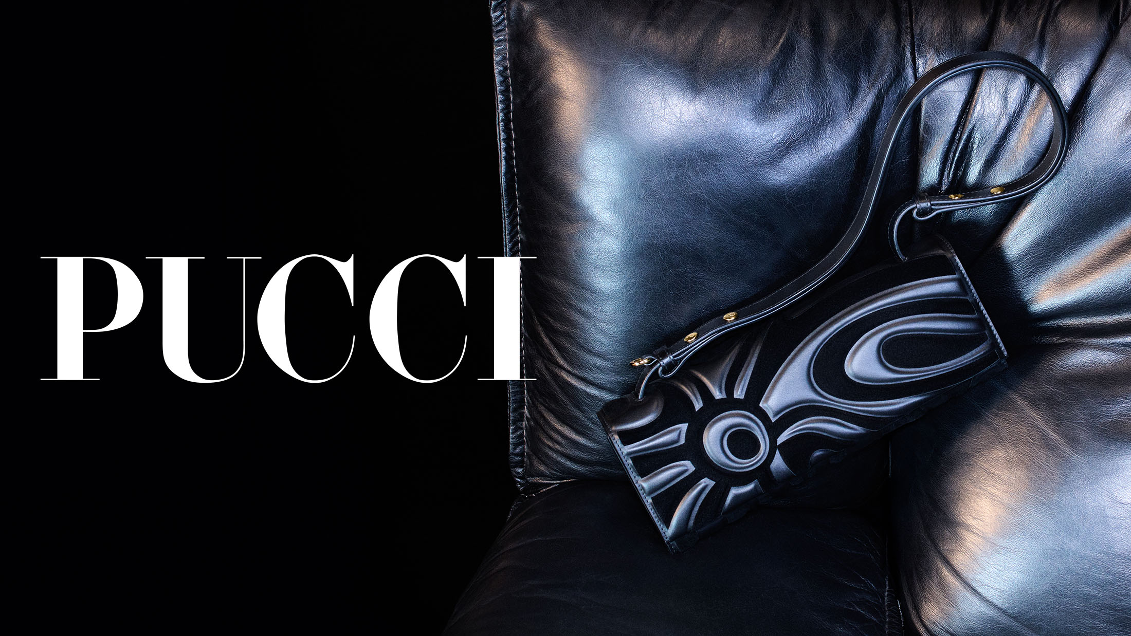 Pucci cylindrical black leather handbag resting against a plush black leather cushion in a dark studio setting