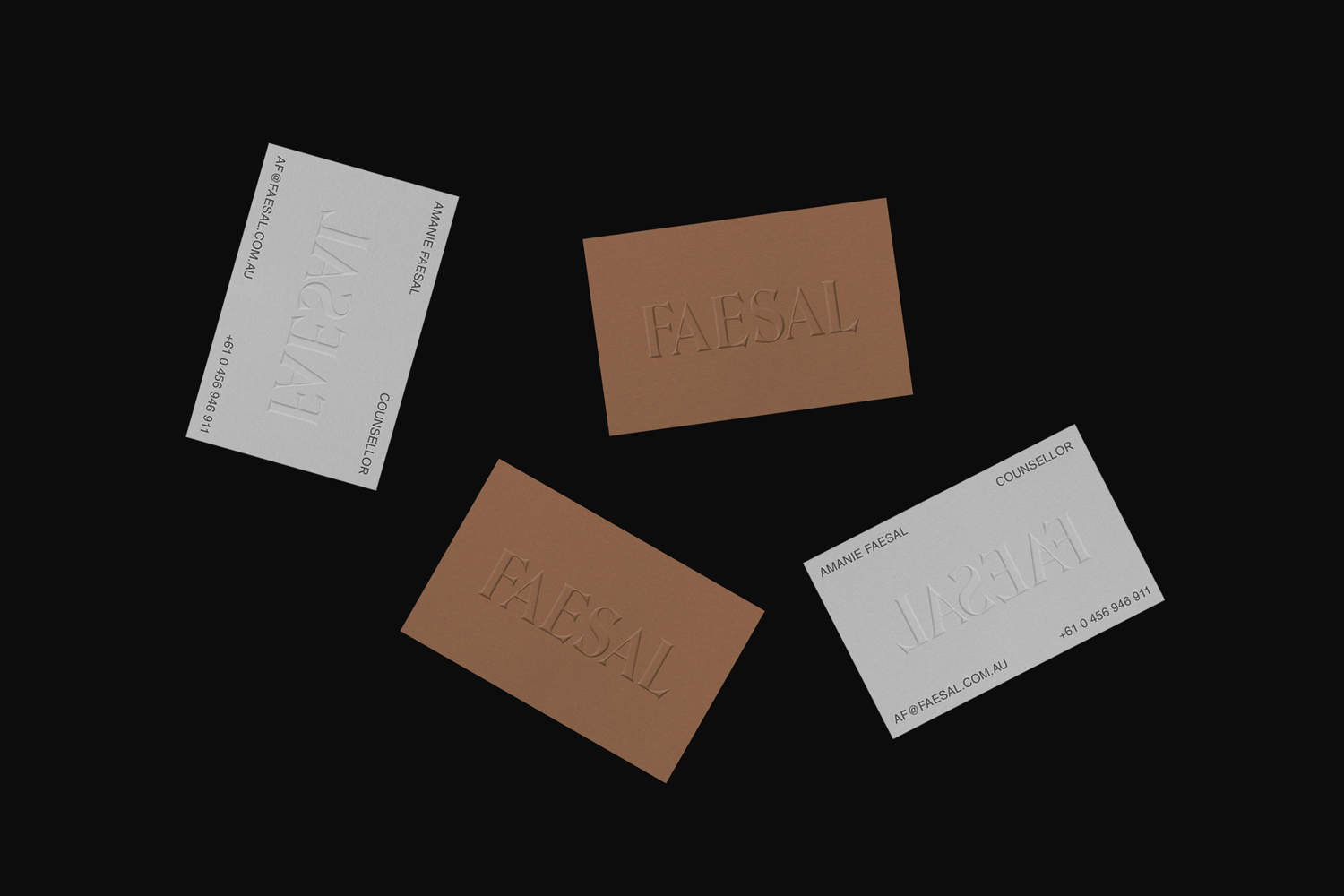 Four rectangular business cards with embossed typography arranged on a dark black background surface