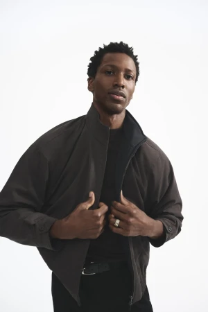 Man wearing a dark jacket standing against a plain white background for the Theory Fall 2025 campaign