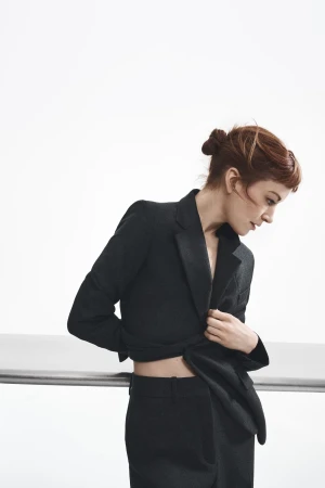 Woman in a black tailored suit leaning against a railing against a plain white studio background