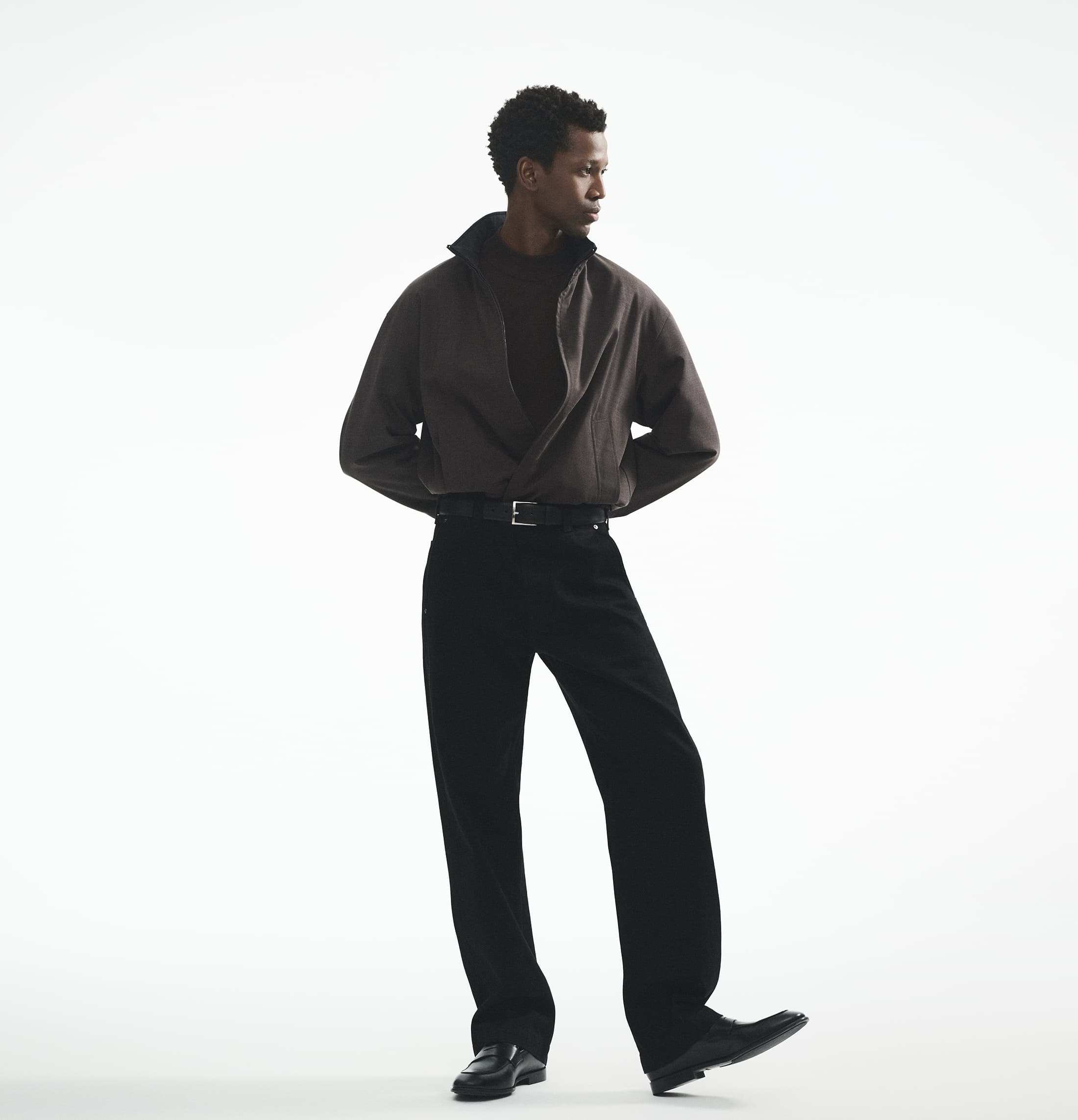 Man wearing a dark jacket and black trousers against a white seamless background for Theory fall 2025 campaign.
